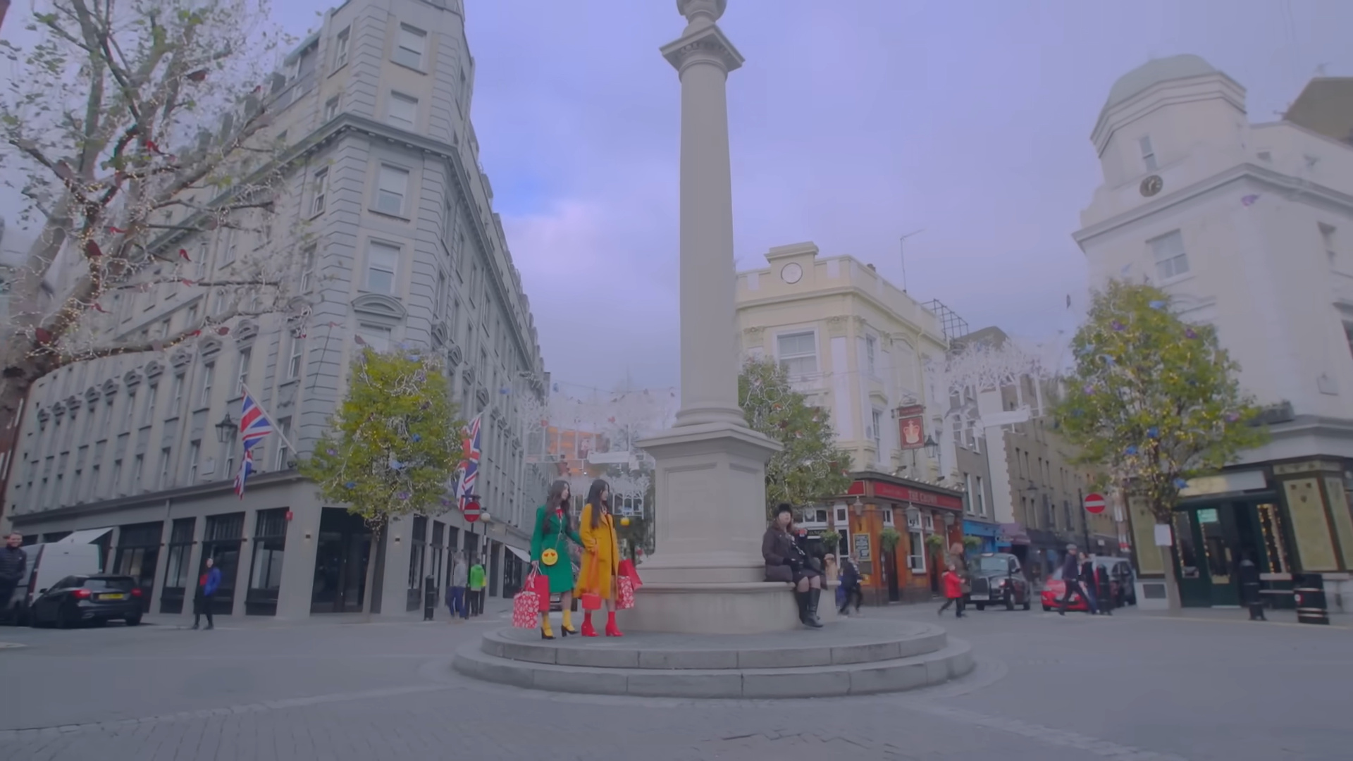 Heejin and Hyunjin walking beside a large monument in a town square.